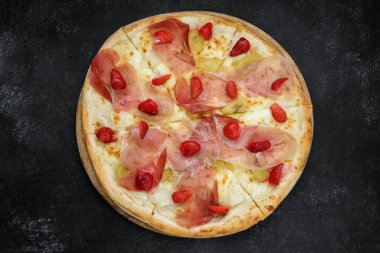 Prosciutto, çilek ve ananas soslu pizza. Gri beton üzerinde ahşap bir tahta üzerinde.