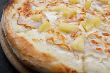 Etli, jambonlu, ananaslı pizza. Gri betondaki ahşap bir tahtanın üzerinde.