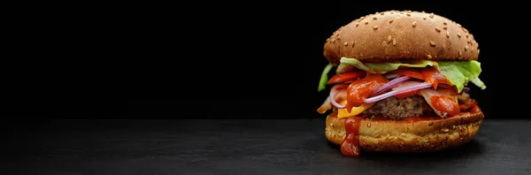 Burger with beef, tomato, lettuce, cheese, ketchup and onion on a black background with place for your text. selective focus