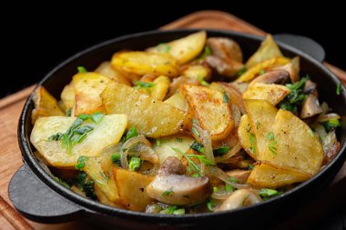 Homemade fried potatoes with mushrooms and onions in a frying pan, on a black background