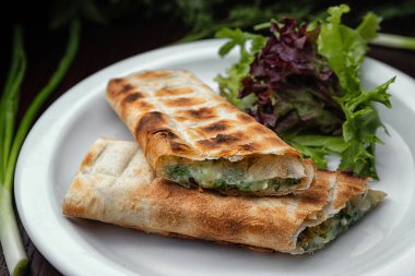 Grilled lavash with suluguni cheese on a white plate with green onions and lettuce