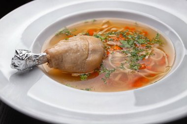 Chicken broth with noodles and chicken leg on a white plate