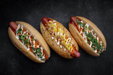 Three hotdogs with different fillings and different sausages on gray concrete