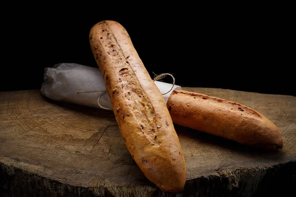 Two white baguette bread on a wooden board on a black background