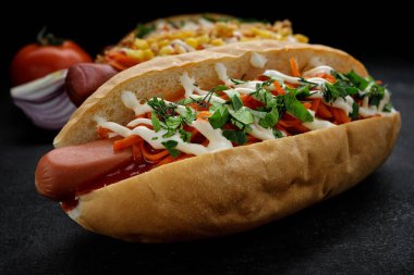 Hot dog with sausage, carrots and dill with parsley close-up on a dark background