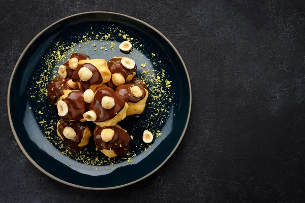 Profiteroles dessert with hazelnuts on a black background. Top view
