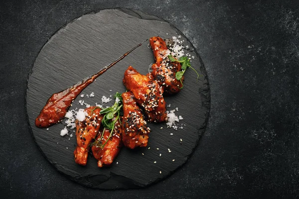 Grilled wings in barbecue sauce on a black round stone