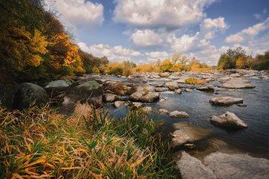 Autumn river with big stones in the water, trees, blue sky and clouds