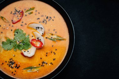Thai soup in a plate with chicken on black stone on gray concrete
