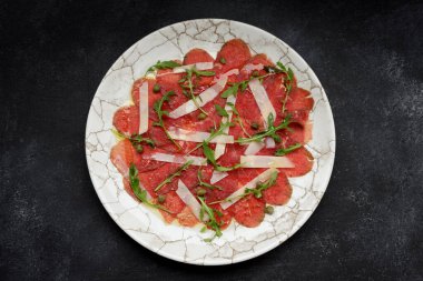 Meat carpaccio with parmesan cheese and arugula, on gray concrete