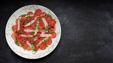 Meat carpaccio with parmesan cheese and arugula, on gray concrete