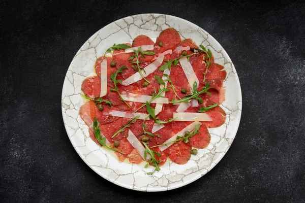 Meat carpaccio with parmesan cheese and arugula, on gray concrete
