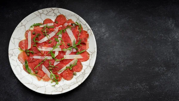 Meat carpaccio with parmesan cheese and arugula, on gray concrete