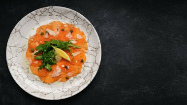 Salmon carpaccio with parmesan cheese, arugula and lemon, on gray concrete