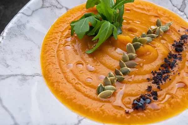 Pumpkin cream soup with seeds and arugula on gray concrete
