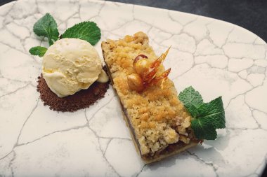 Piece of pie with apples and ice cream on a white plate with mint