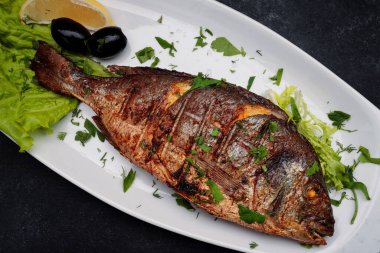 Dorado fish grilled with herbs, on a plate, on a dark background