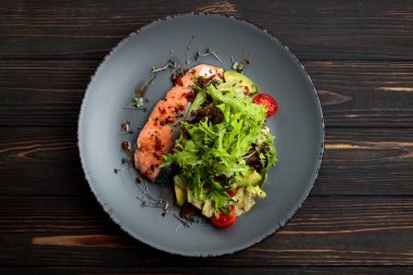 Grilled salmon fillet with vegetables and salad leaves on a wooden background