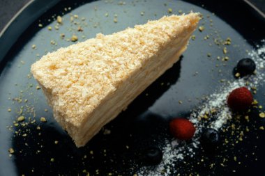 Piece of Napoleon cake with berries, on a plate, on a dark background