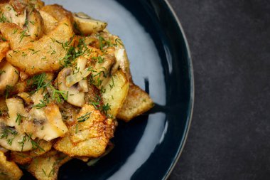 Fried potatoes with mushrooms and herbs on a plate, on gray concrete