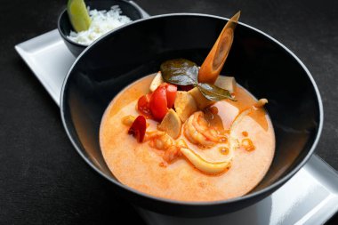 Tay çorbası, deniz ürünleri, pirinç ve domates, bir tabakta, koyu beton üzerinde.