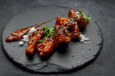 Siyah taşın üstünde ızgara tavuk kanatları, gri betonun üzerinde mikroyeşil