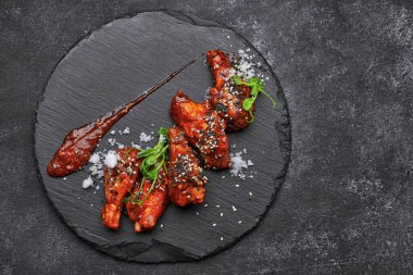 Siyah taşın üstünde ızgara tavuk kanatları, gri betonun üzerinde mikroyeşil