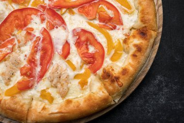 Sebzeli pizza, tavuk ve peynir tahtanın üstünde, koyu betonun üzerinde.