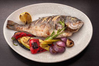Ahşap arka planda ızgara sebze ve limonla ızgara dorado balığı.