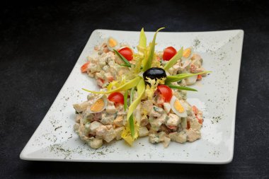 Beyaz tabakta koyu betonda Olivier salatası.