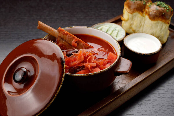 Украинский борщ со сметаной и пончики с чесноком, на деревянной доске, на темном фоне