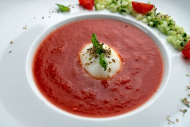 Tahta arka planda beyaz bir tabakta domates çorbası, domates ve otlarla.