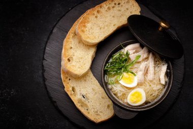 Yumurtalı tavuk çorbası ve kızarmış ekmek, dökme demir bir tencerede, gri betonun üzerinde.