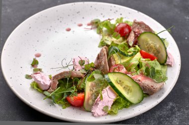 Buzağı ve krem peynirli sıcak salata, beyaz tabakta ve koyu arka planda.