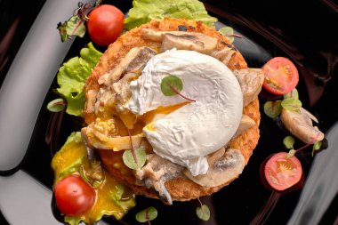 Mantarlı biftek, haşlanmış yumurta ve domatesler siyah tabakta, siyah arka planda.