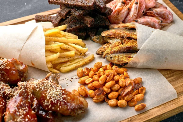 Snack to beer, on a wooden board. Shrimp. Fried fish. Fried peanuts. Chicken wings, Croutons