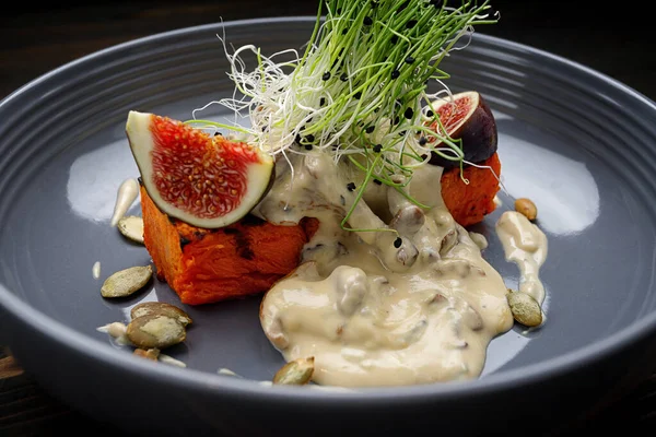 Grilled pumpkin with mushroom sauce with microgreens, on a wooden background