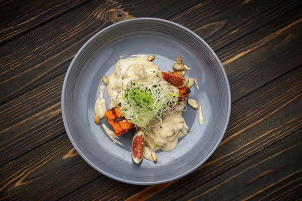 Grilled pumpkin with mushroom sauce with microgreens, on a wooden background