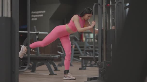 젊은 여자가 넓적다리와 다리 근육을 훈련시키기 위해 다리를 드는 크로스오버를 하고 있다. 엉덩이 훈련. 전문 여성 운동 선수는 다리 운동을 한다 — 비디오