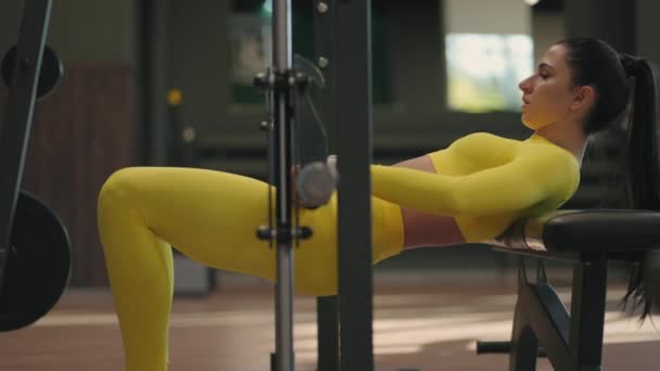 노란 트럭 수트 를 입은 한 젊은 여인 이 넓적다리와 엉덩이의 뒷부분을 훈련시키기 위하여 바벨 로 몸을 들어올리고 있다. 스미 소니 시뮬레이터 에서의 역도 훈련. 헬스클럽에서 체중으로 허리와 몸을 펴는 모습 — 비디오