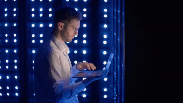 Mężczyzna inżynier sieci robi kontrolę systemu stojąc w serwerowni z laptopem. W centrum danych mężczyźni serwer specjaliści sprawdzanie systemu pracy i sprzętu szafy serwerowe rack — Wideo stockowe