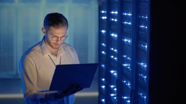 Man Server Engineer in het datacenter. IT-ingenieur inspecteert een beveiligde serverkast met behulp van moderne technologie laptop coworking in datacenter. — Stockvideo