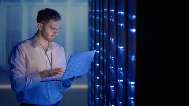 Man Server Engineer in het datacenter. IT-ingenieur inspecteert een beveiligde serverkast met behulp van moderne technologie laptop coworking in datacenter. — Stockvideo