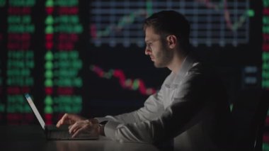 Genç Kafkasyalı tüccar bilgisayar monitöründe çalışıyor ve ticaret ofisinde internette geziniyor. Erkek komisyoncu oranları ve bahisleri takip ediyor. Ekranda yönetici mesajı.