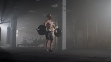 Yakışıklı kaslı adam ağırlık kaldırıyor ve halterle kıvırıyor. Atletik Üstsüz Adam Eğitimi, Güç Kullanımı, Güç ve Dayanıklılık Halterleri. Hardcore Spor Salonu 'nda egzersiz
