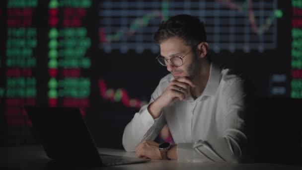 Un profesional con gafas mira la pantalla del monitor de la computadora y piensa en analizar el mercado de valores. Brooding desconcertado corredor espera el crecimiento de las acciones — Vídeos de Stock