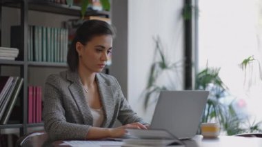 Laptopta yazı yazan İspanyol kadının portresi, müşteriye e-posta gönderiyor ve sonuçtan memnun. İş kadını masada oturuyor.