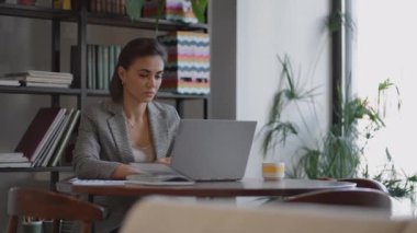 Laptopta yazı yazan İspanyol kadının portresi, müşteriye e-posta gönderiyor ve sonuçtan memnun. İş kadını masada oturuyor.