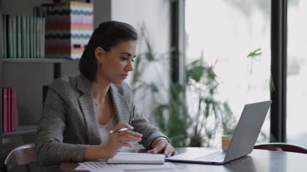 Donna d'affari che scrive qualcosa nel quaderno. Studente imprenditrice start-up che studia scrittura sul posto di lavoro vicino al computer. Una mano di donne che scrive su un quaderno bianco bianco sul tavolo . — Video Stock