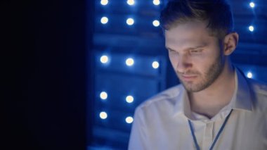 Sunucu odasında dizüstü bilgisayarla çalışan bir adamın portresi. Teknisyen sunucu odasında check-up yapıyor. Beyaz mühendis gri işçi ceketi giyiyor.